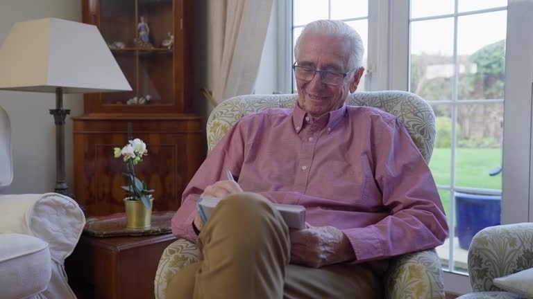 Senior Man Sitting In Armchair At Home Enjoying Sudoku Puzzle Book