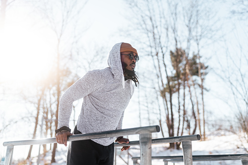 A man in his thirties working out at an outdoor gym. It's a sunny winter day in Sweden. The gym in the public park is covered in snow.