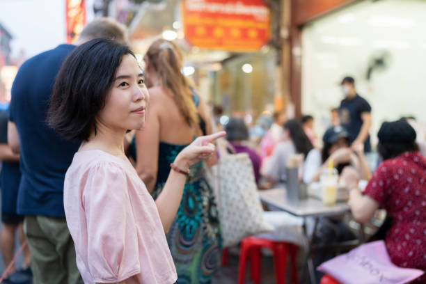 Explore your eyes in famous place at Bangkok Thailand. Asia woman traveling at Yaowarat street food in Bangkok. Woman standing on the road and point to the crowded resturant at night market. Enjoy food and take a long queue explore sus ojos en un lugar famoso en bangkok, tailandia. mujer asiática viajando en la comida callejera yaowarat en bangkok. mujer parada en la carretera y señalando el restaurante lleno de gente en el mercado nocturno. disfruta de la comida y haz una