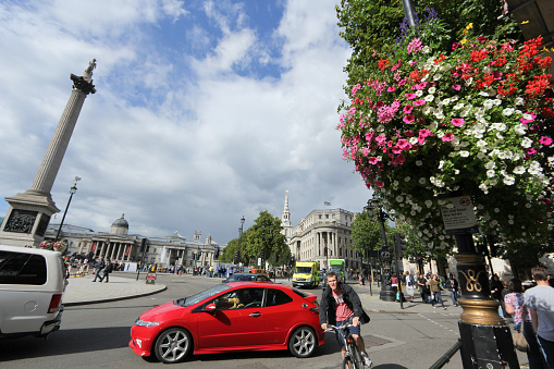 London, England - August 27, 2011: A cyclist cycles towards the photographer as cars drive past in the traffic circle near Trafalgar Square, a popular travel destination in the UK. Identifiable pedestrians walk past on the pavement.