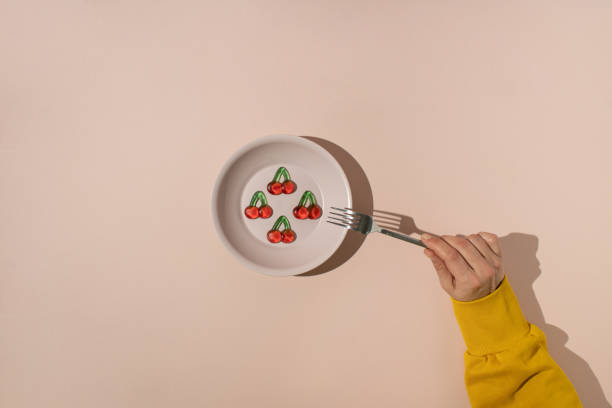 istock Hand with fork reaching for gummy candies shaped like cherries served in plastic plate on beige background. 1473225396