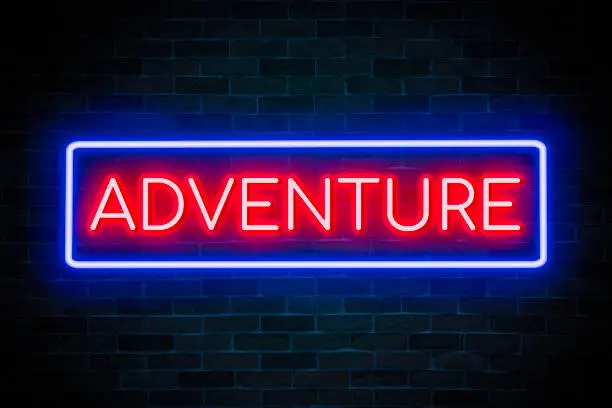 Photo of Adventure text neon banner on brick wall background.