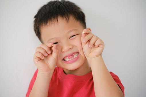 Cute Asian happy smiling schoolboy child showing missing teeth, Little kid losing his baby teeth and holding missing tooth, Dental care for children concept