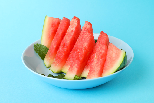 Plate with watermelon slices and mint leaves on blue background