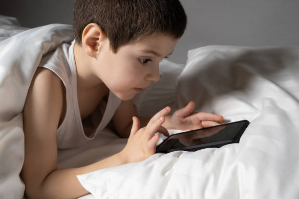 istock A 5 year old boy plays games on his phone while lying in bed. Gadgets in bed before bedtime in a child 1473230937