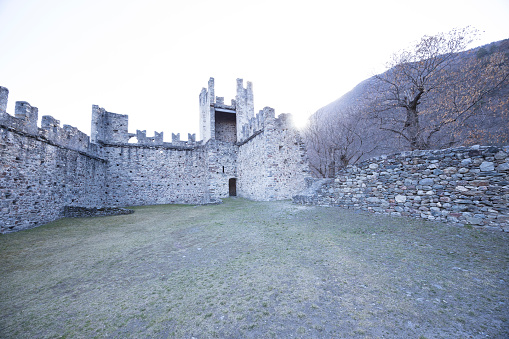 Valtellina, Italy - March 12, 2023: street view of the ancient walls surrounding Old Castle in Grosio, a fort in ruins. No people are visible, background is the mountains of Valtellina.