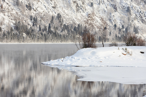 Winter landscape with Yenisei river. Frosty snowy forest on the rocky shore. Snow mountain landscape in winter scenery