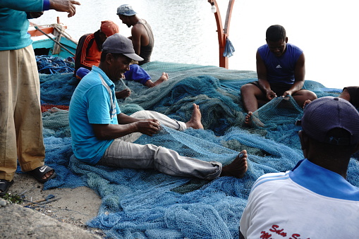 Some fishermen focused on repairing trawl nets torn by corals while fishing. Fixing a broken trawl net is an important task. This activity requires patience and accuracy to extend the life of the net and maintain the quality of fish catches in the sea around the Gampong Lampulo fishing boat port, Banda Aceh, Indonesia on March 07, 2023