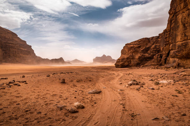 clouds of sand blow around rocks in the midst of a vast sand desert - fog desert arabia sunset imagens e fotografias de stock