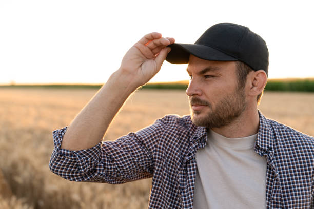 Bearded farmer in a cap and a plaid shirt against the background of a field