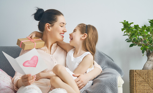 Happy women's day! Child daughter is congratulating mom and giving her postcard and gift. Mum and girl smiling and hugging. Family holiday and togetherness.