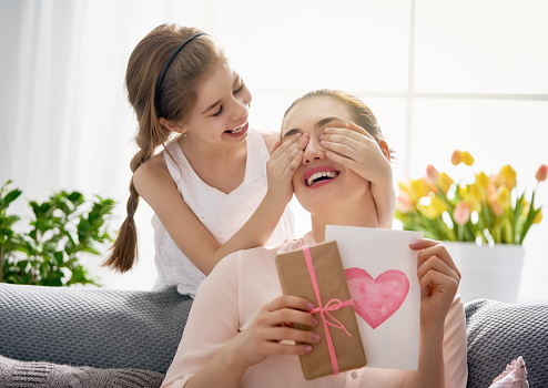 Happy women's day! Child daughter is congratulating mom and giving her postcard and gift. Mum and girl smiling and hugging. Family holiday and togetherness.