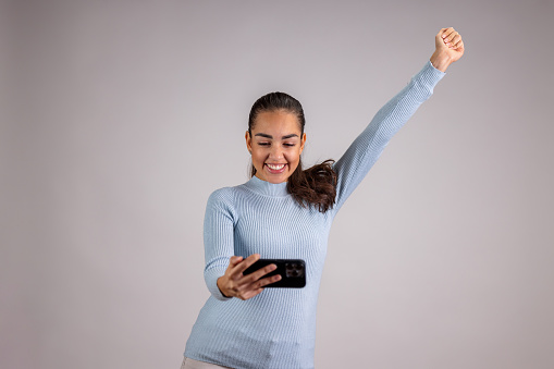 Hispanic Woman Holding Her Smart Phone,  Cheering And Laughing