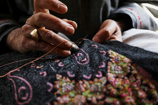 Creating art with every stitch - a master artisan delicately sewing intricate designs onto a Kashmiri shawl, transforming soft wool into a timeless masterpiece.