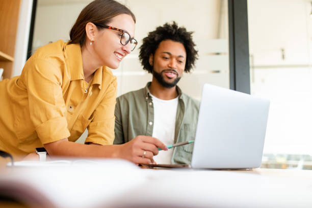 istock Two colleagues have pleasant conversation sitting side by side in modern open space office, smiling and enjoying friendly working atmosphere 1473244861
