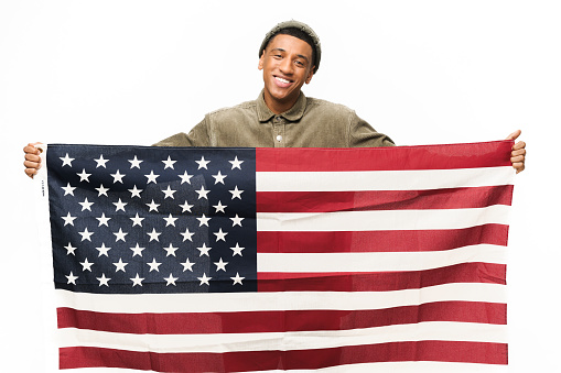 Cheerful African-American guy holding in hands american flag, looking at the camera and smiling isolated on white background, Flag Day concept