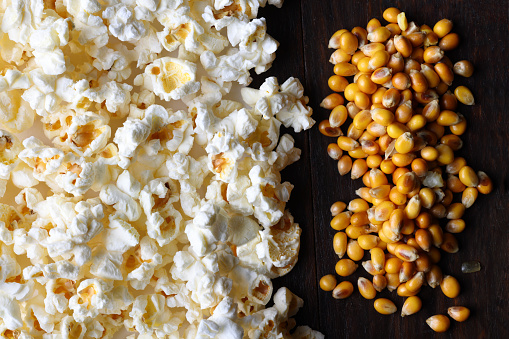 A bowl of popcorn with cobs of fresh corn on a dark background. Copyspace