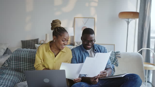 Young smiling couple working from home, going over paperwork while sitting on the sofa