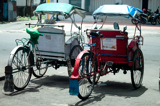 Ambon, Indonesia - March 12, 2023 : two red and white rickshaws parked beside the main road