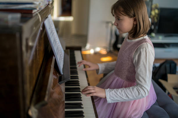 Cute girl playing piano at home Side view of girl playing piano. Cute female child is practicing on musical instrument. She is at home. girl playing piano stock pictures, royalty-free photos & images