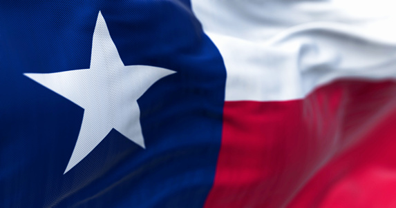 The Texas state flag fluttering in the wind. Blue vertical stripe with white star, white and red horizontal stripes. 3D illustration render. Selective focus. Close-up. Rippled textile background