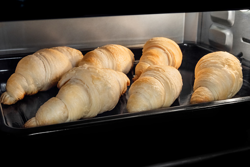 Six croissants baking and rising on tray in electric oven. French cuisine, homemade bakery, breakfast, food, cooking and pastry concept