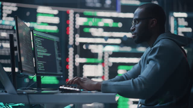 Dolly Shot of a Black Male Programmer Working in a Monitoring Control Room, Surrounded by Big Screens Displaying Lines of Programming Language Code. Portrait of a Man Creating a Software and Coding