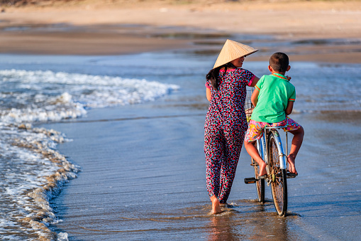 Vietnamese mother with a bicycle on the beach, Vietnam
