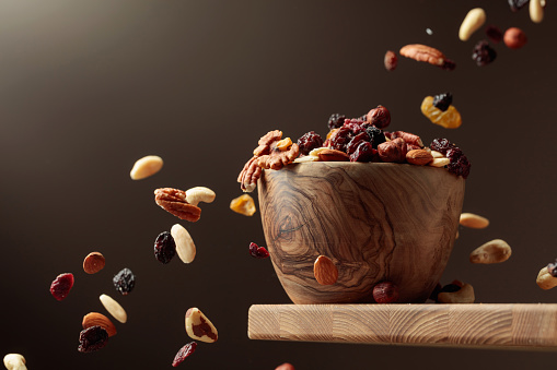 Flying dried fruits and nuts. The mix of nuts and dried berries are in a wooden bowl.