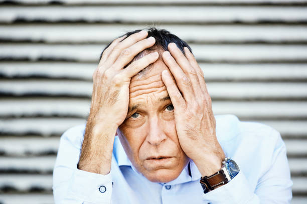 Man in his 50s, dressed in a smart shirt, seems overcome by shock, worry and anxiety.