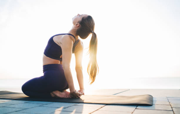 Sportswoman stretching body on quay in sunshine Side view of flexible barefoot lady performing Thunderbolt pose with hands together behind back and bending back during workout on beach hands behind back stock pictures, royalty-free photos & images