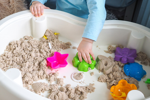 Faceless baby boy is playing with kinetic sand and colorful molds on the table. Concept of Home Early Education, Preparing for School, sensory activity, therapy.