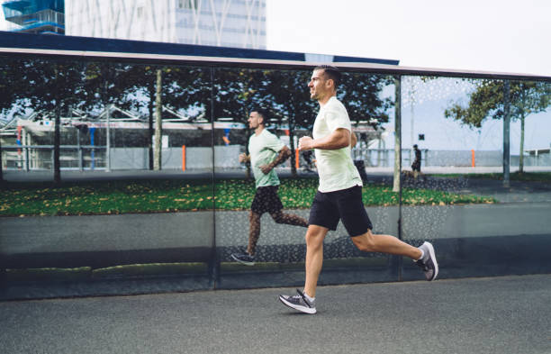 マラソンの準備をしている決然とした男性アスリートの側面図は、都市都市部で有酸素運動の朝のトレーニングを受け、スポーツウェアを着たやる気のある男性が健康的なライフスタイルを� - marathon sport sports training city street ストックフォトと画像