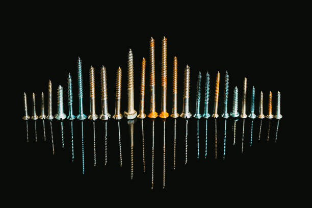 A collection of screws in a row, standing up so that they resemble the skyline of a modern city with towers and skyscrapers. The screws are reflected on a shiny black surface.
