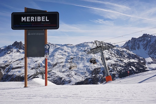 Meribel, France - 6 March 2023: Looking at a signpost for the Meribel section of the Three Valleys ski area on the ridge crossing from St Martins and Les Menuires.  Behind is the the top of the Tougnete 2 ski lift.