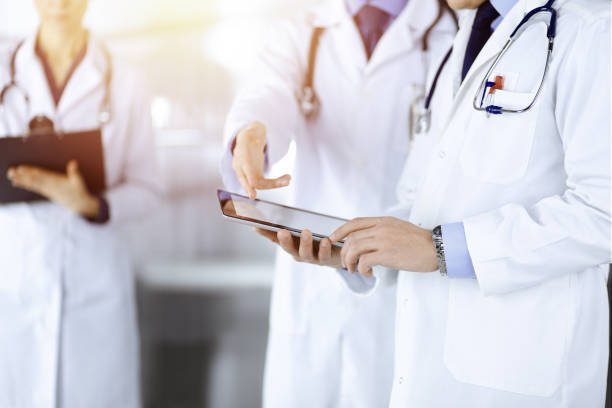 istock Group of unknown doctors use a computer tablet to check up some medical names records, while standing in a sunny hospital office. Physicians ready to examine and help patients. 1473273294