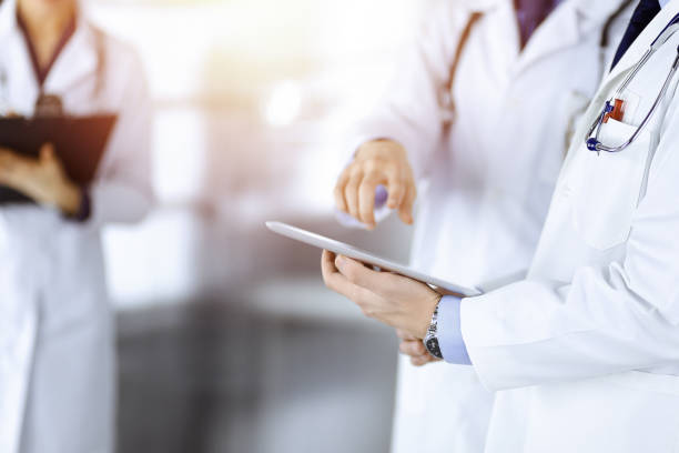istock Group of unknown doctors use a computer tablet to check up some medical names records, while standing in a sunny hospital office. Physicians ready to examine and help patients. 1473273300