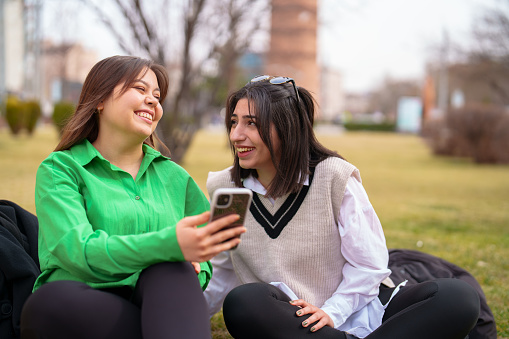 Two young female using mobile devices outdoors