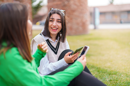 Two young female using mobile devices outdoors