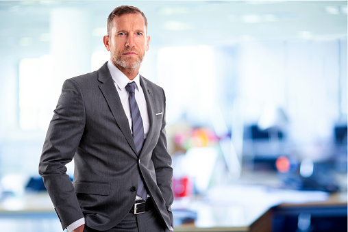 Portrait of serious faced businessman looking at camera and standing in a boardroom. Confident mature male professional is wearing suit.