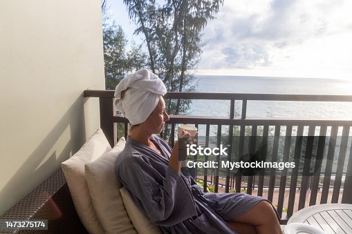 istock Woman enjoying luxury hotel, she relaxes on her balcony looking out at sea 1473275174