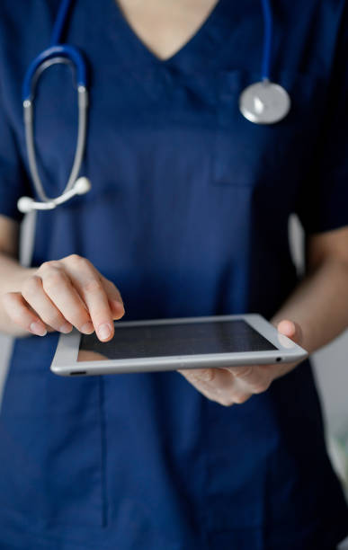istock Doctor woman using tablet computer while standing near panorama window in clinic, close up. Physician or surgeon at work. Medicine concept 1473276888