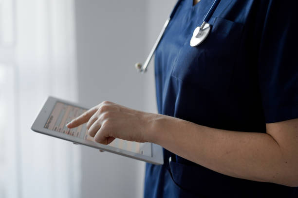 istock Doctor woman using tablet computer while standing near panorama window in clinic, close up. Physician or surgeon at work. Medicine concept 1473276893