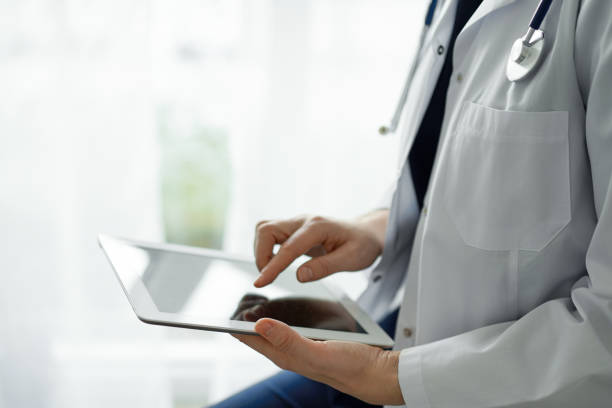istock Doctor woman using tablet computer while standing near panorama window in clinic, close up. Physician or surgeon at work. Medicine concept 1473276894