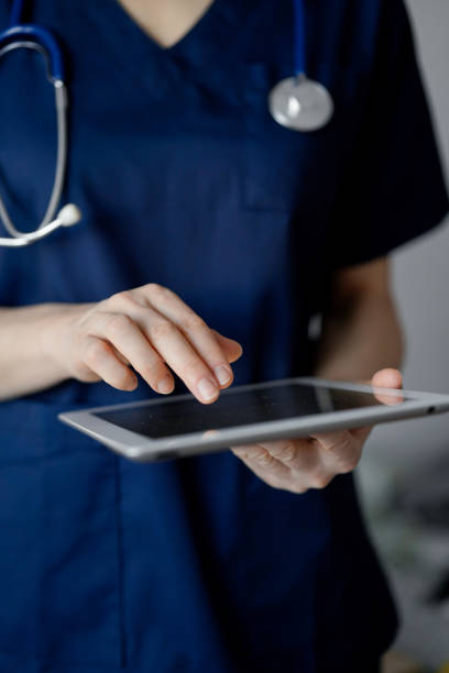 istock Doctor woman using tablet computer while standing near panorama window in clinic, close up. Physician or surgeon at work. Medicine concept 1473276906