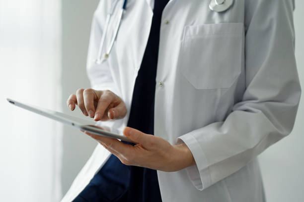 istock Doctor woman using tablet computer while standing near panorama window in clinic, close up. Physician or surgeon at work. Medicine concept 1473276932