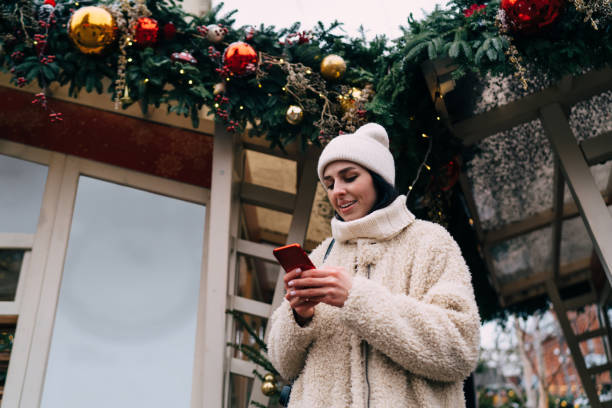 istock Content lady using smartphone near building with Christmas decorations 1473277566