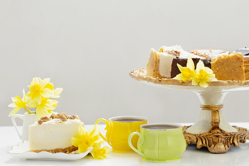 cheesecake with cup of coffee and yellow spring flowers on white table