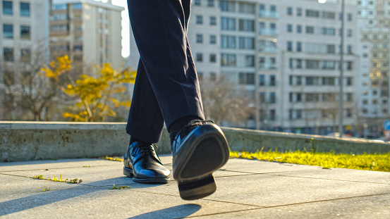 Legs of a businessman in fashionable shoes walking outdoors. Business concept. Close-up view to the businessman in a black new shoes walks on the street. Stylish men wears. Low angle