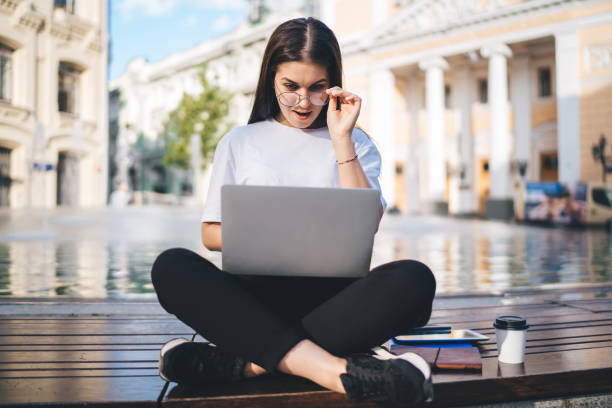 istock Amazed hipster girl in optical eyewear shocked with received email message on modern netbook technology, impressed digital nomad reading blog publication using public internet connection in city 1473282491